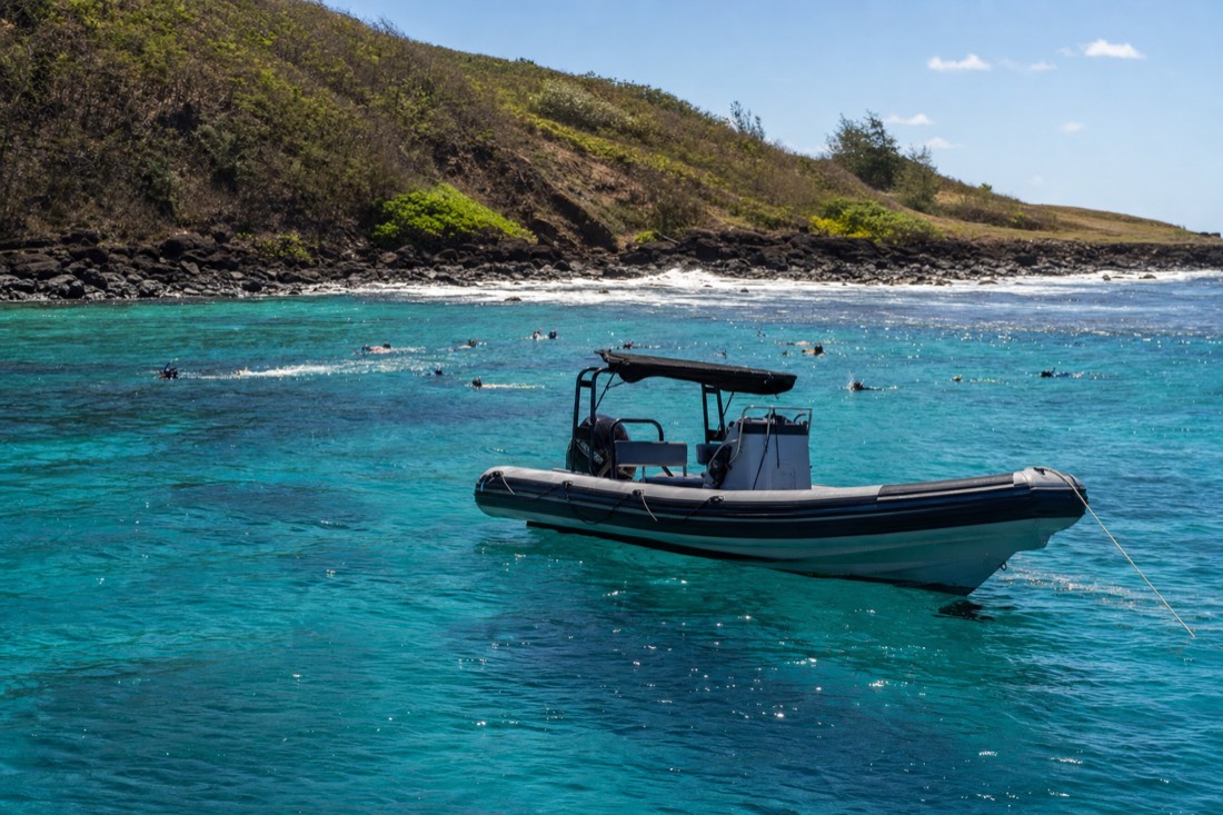 A zodiac boat and snorkelers over a reef in clear turquoise water off Kauai's south shore