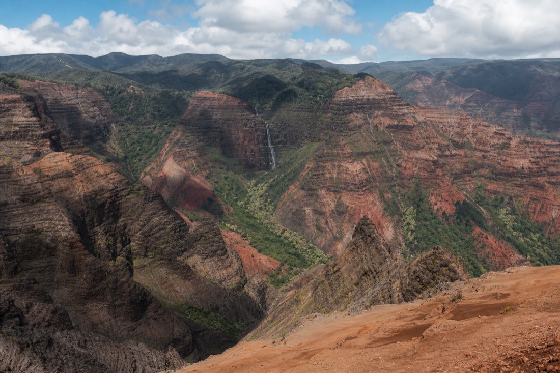 Waimea Canyon's red gorge and green ridgelines on Kauai, seen from a lookout on a canyon tour